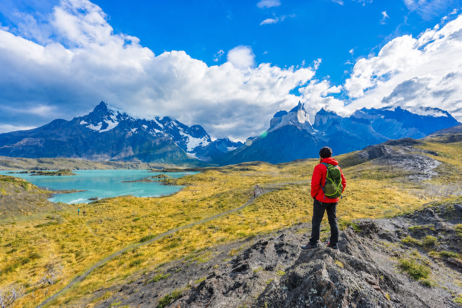 Person standing on a rocky outcrop overlooking a scenic landscape with mountains and a lake.